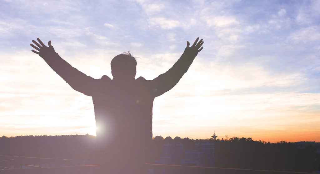 Man facing sunrise with arms outstretched